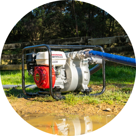 Honda water pump in use outdoors, transferring water with a wooden fence in the background